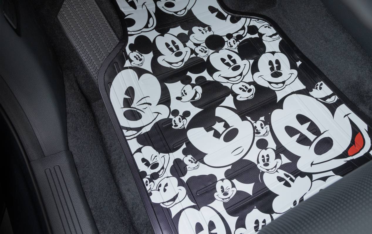 A car seat cover patterned with multiple black and white images of Mickey Mouse in various expressions and poses, set against the interior of a vehicle.