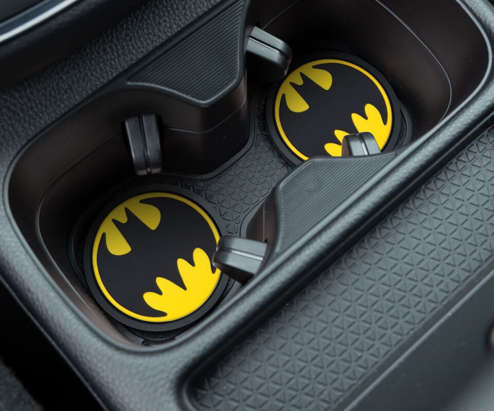 Car cup holders with Batman logo coasters, situated in a textured vehicle center console.