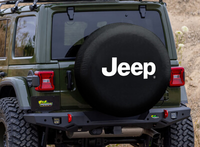 A spare tire cover with the logo "Jeep" mounted on a green SUV, likely a Jeep, with a focus on the vehicle's rear.