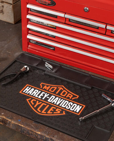 A red tool chest with drawers sits next to a black mat featuring the "Harley-Davidson Motor Cycles" logo, with wrenches laid upon it, in a workshop setting.